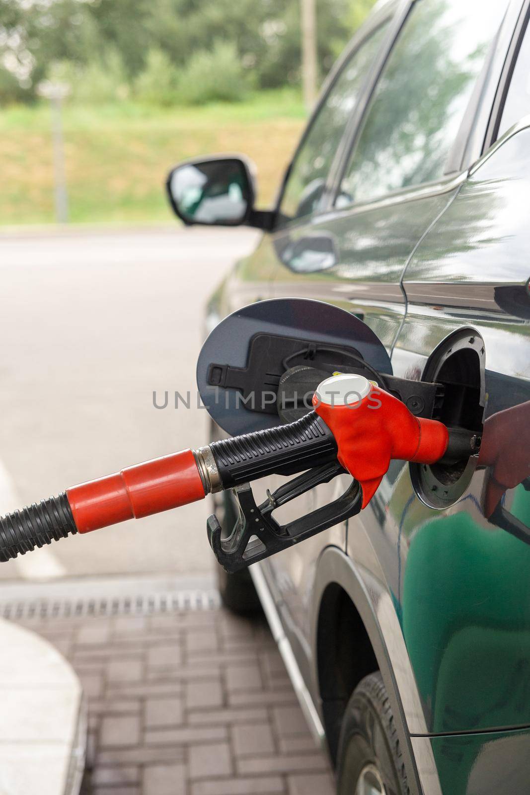 Fuel nozzle to refill fuel in car at gas station. Red fuel dispenser on gray car in petro station.