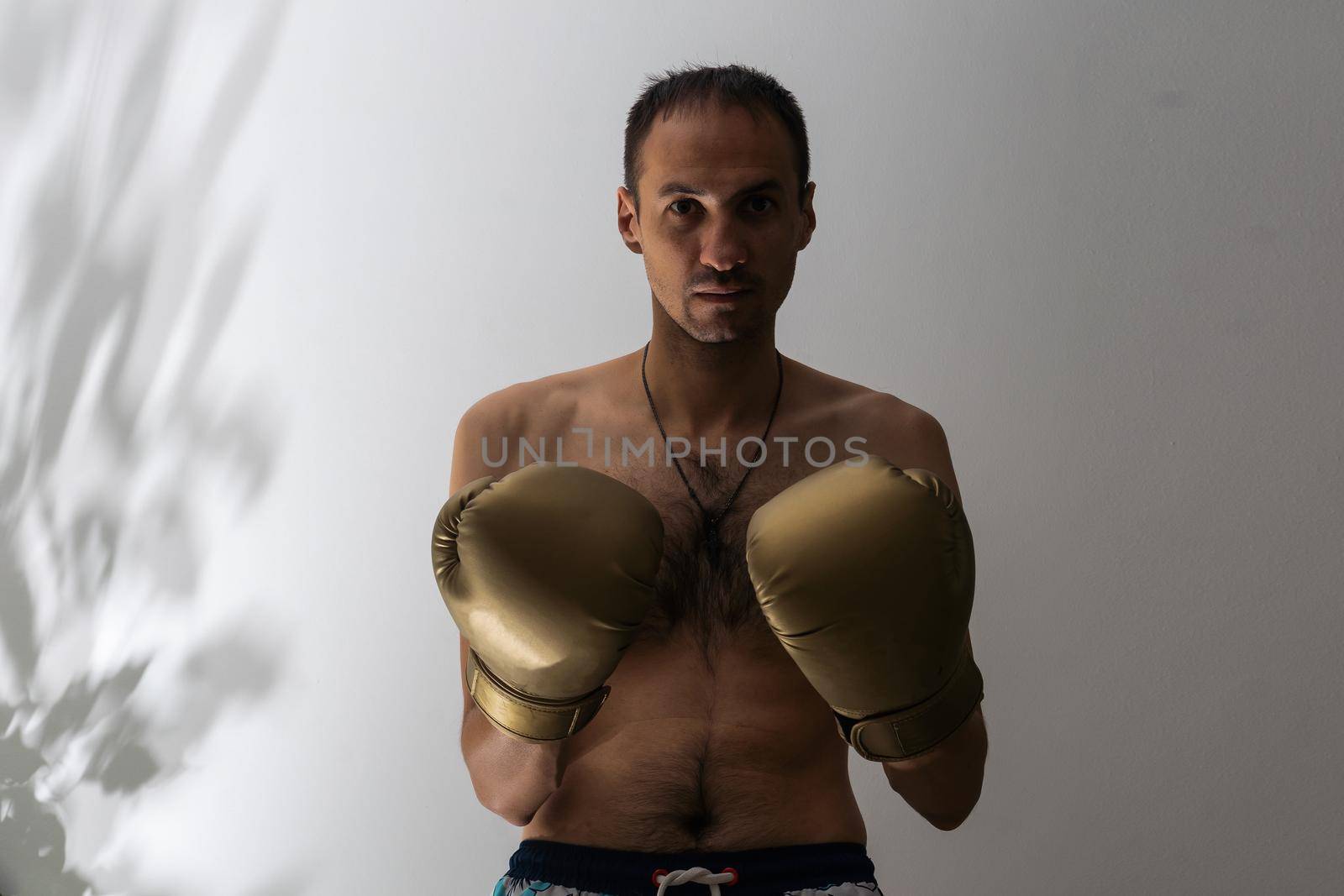 closeup shot of young naked boxer wearing protecting gloves. throwing puches in a boxing ring. grey background by Andelov13