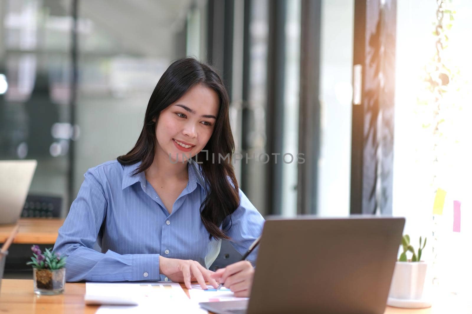 Happy young Asian businesswoman working on laptop and taking notes In office..