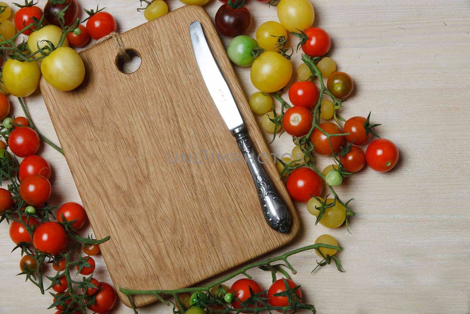 Little red, yellow, green and black cherry tomatoes on white table with wooden cutting board in the middle, place for text, flat lay. by Vera_FoodandGarden