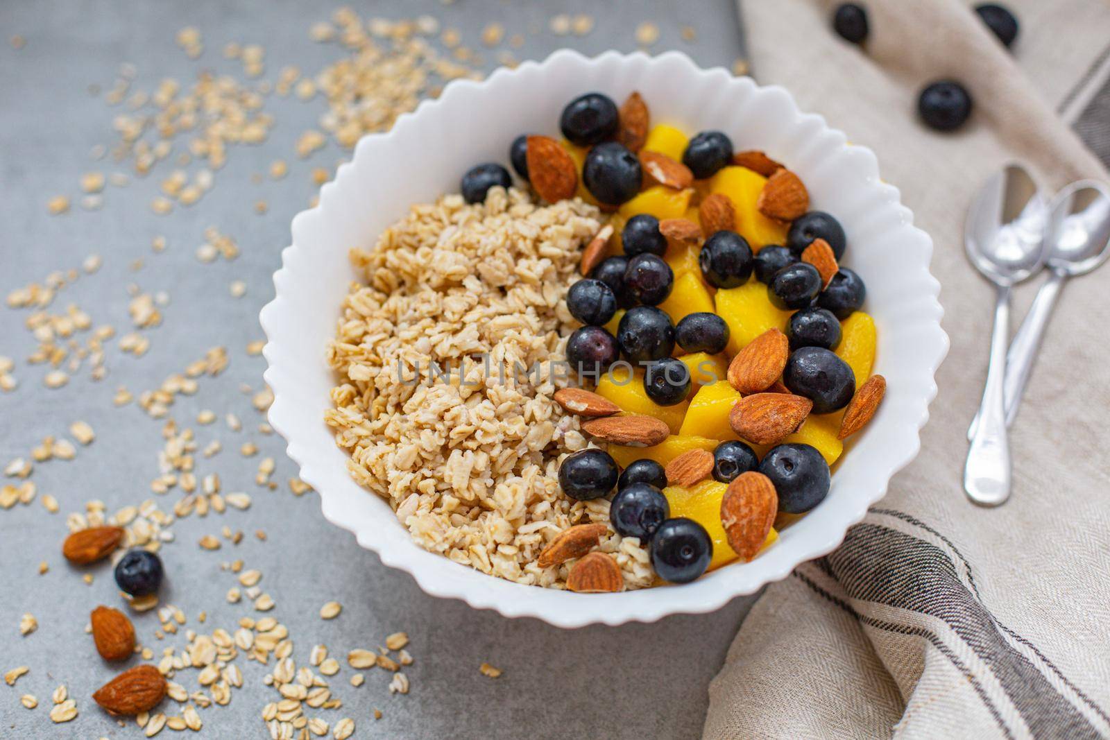 Oatmeal porridge with blueberries, mango and almonds in bowl on concrete grey table from above. flatlay. Healthy breakfast food. Copy space