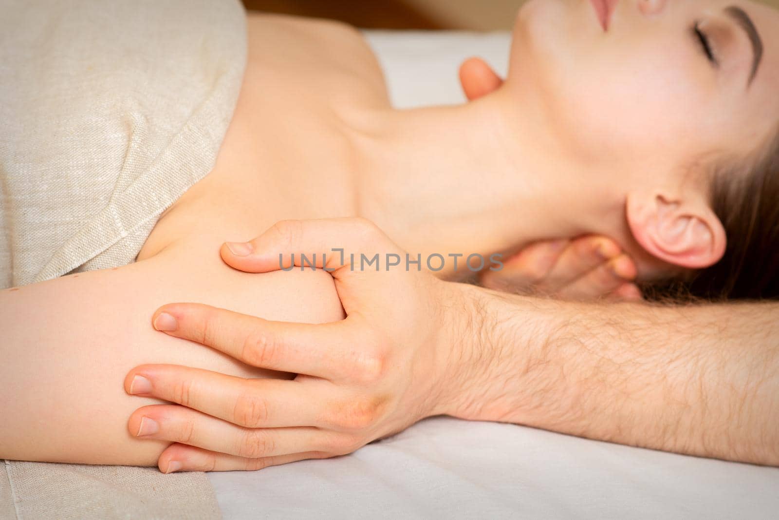 Male masseur massaging shoulder of a young woman lying on a massage table in a spa clinic