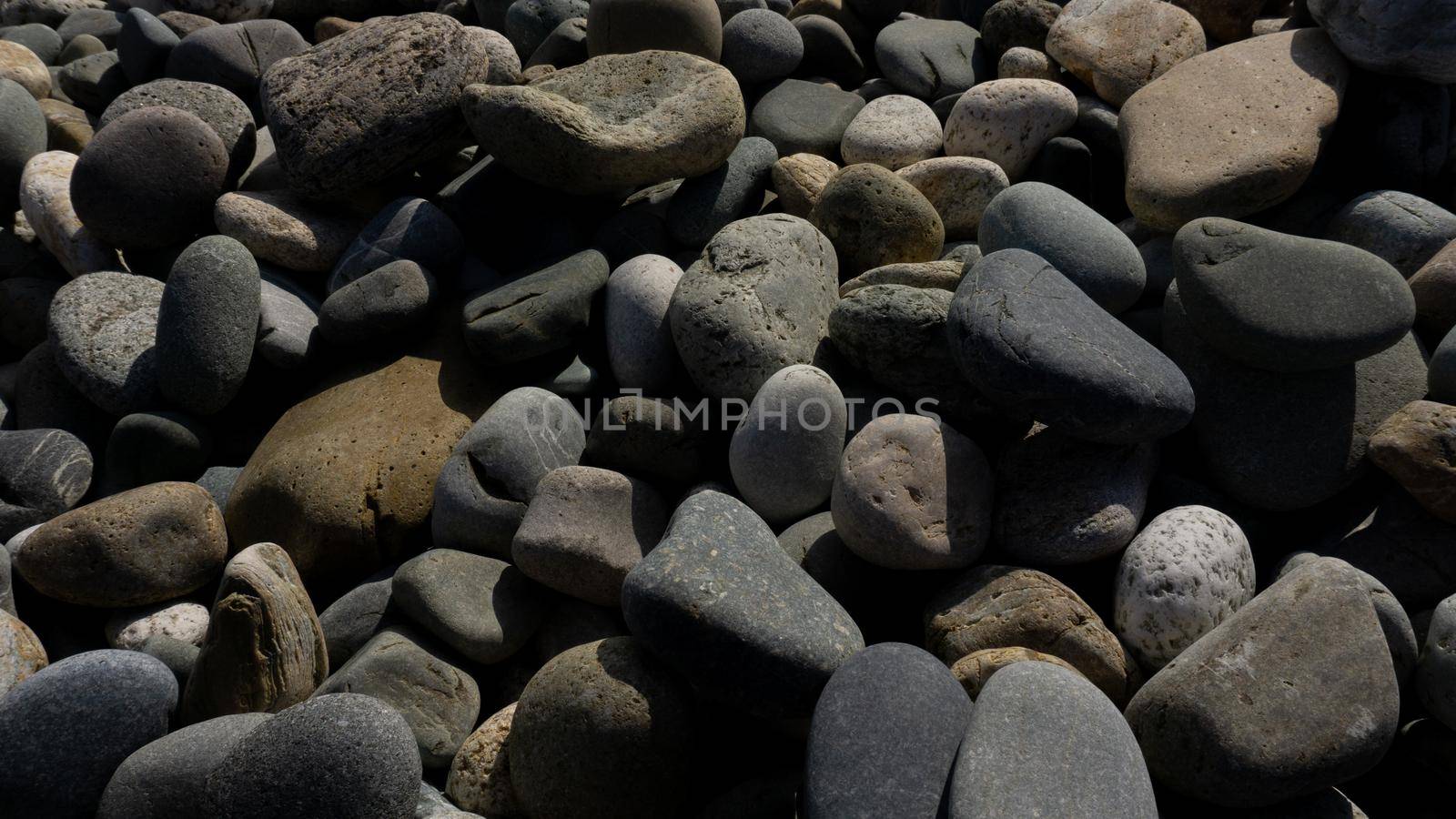 Sea stones background with small pebbles or stone in garden or in the seaside or on a beach. Close up view of rounded smooth polished pebble stones.