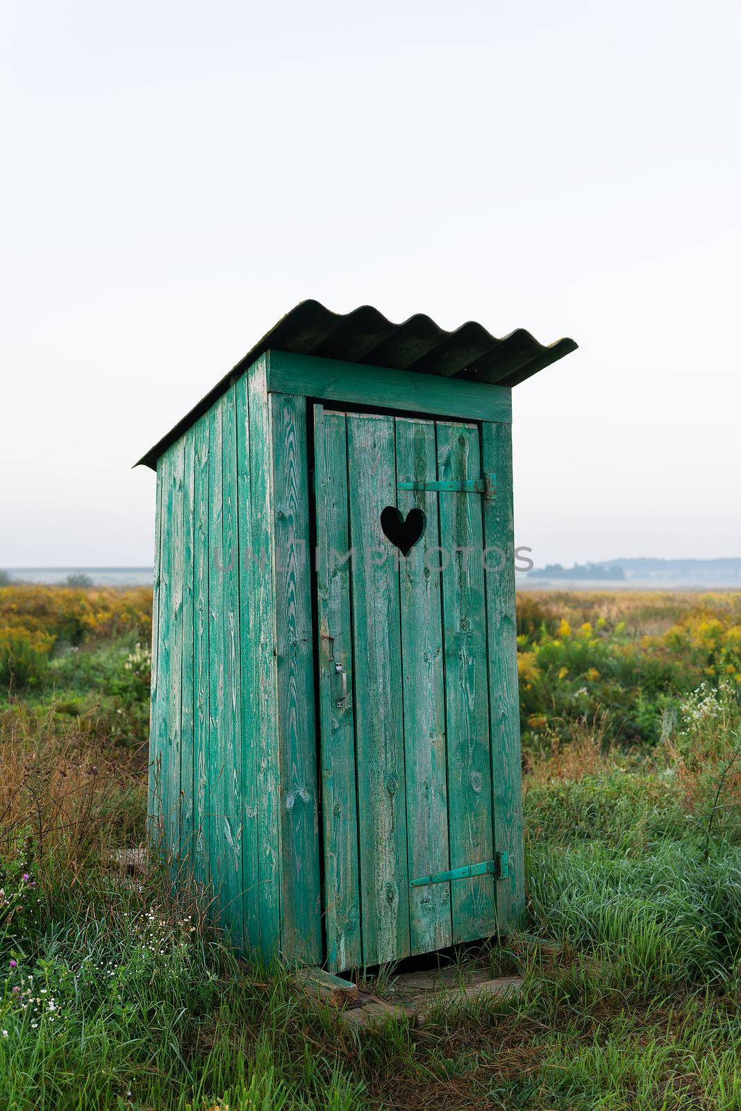 Heart shape on the old wooden toilet door, green toilet in the field. Outdoor recreation