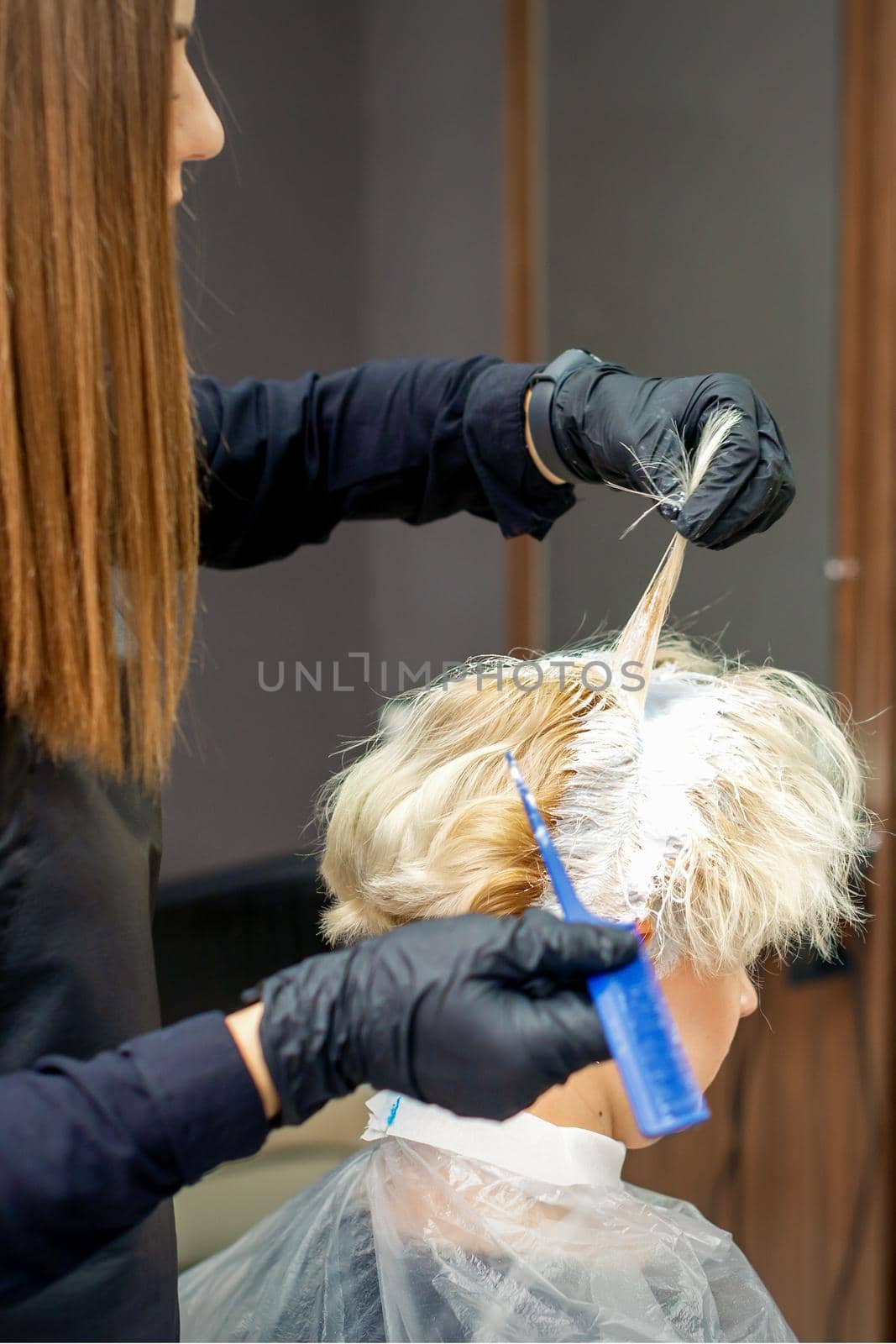 Coloring female hair in the hair salon. Young woman having her hair dyed by beautician at the beauty parlor. by okskukuruza