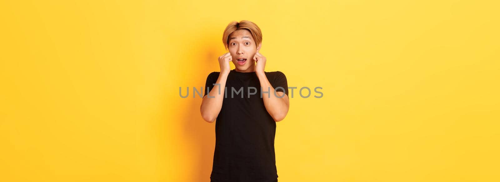 Excited handsome blond guy in black clothes, looking tempted and standing over yellow background by Benzoix
