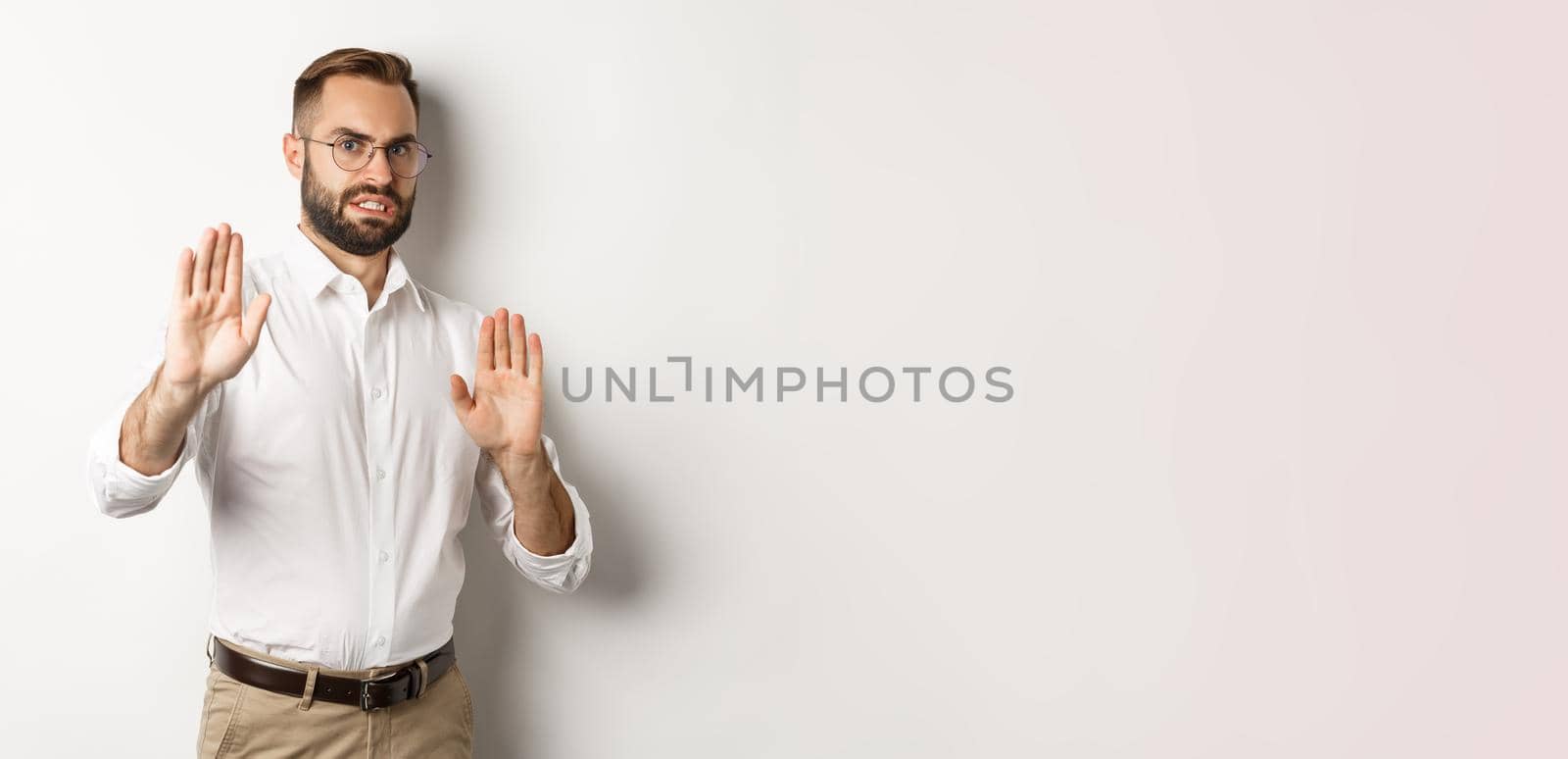 Displeased man rejecting something disturbing, showing stop sign and declining, cringe from aversion, standing over white background by Benzoix