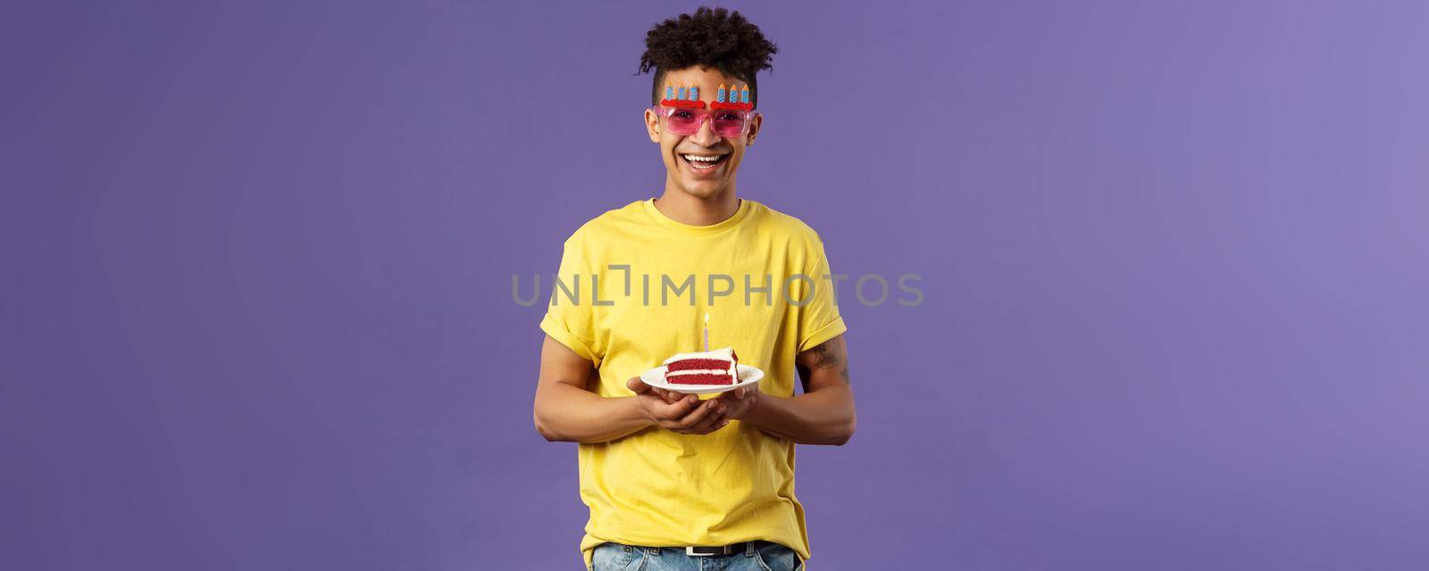 Celebration, party and holidays concept. Portrait of upbeat, charismatic lively man with dreads, hipster guy wearing funny glasses mask celebrating birthday, have fun, hold cake with candle.