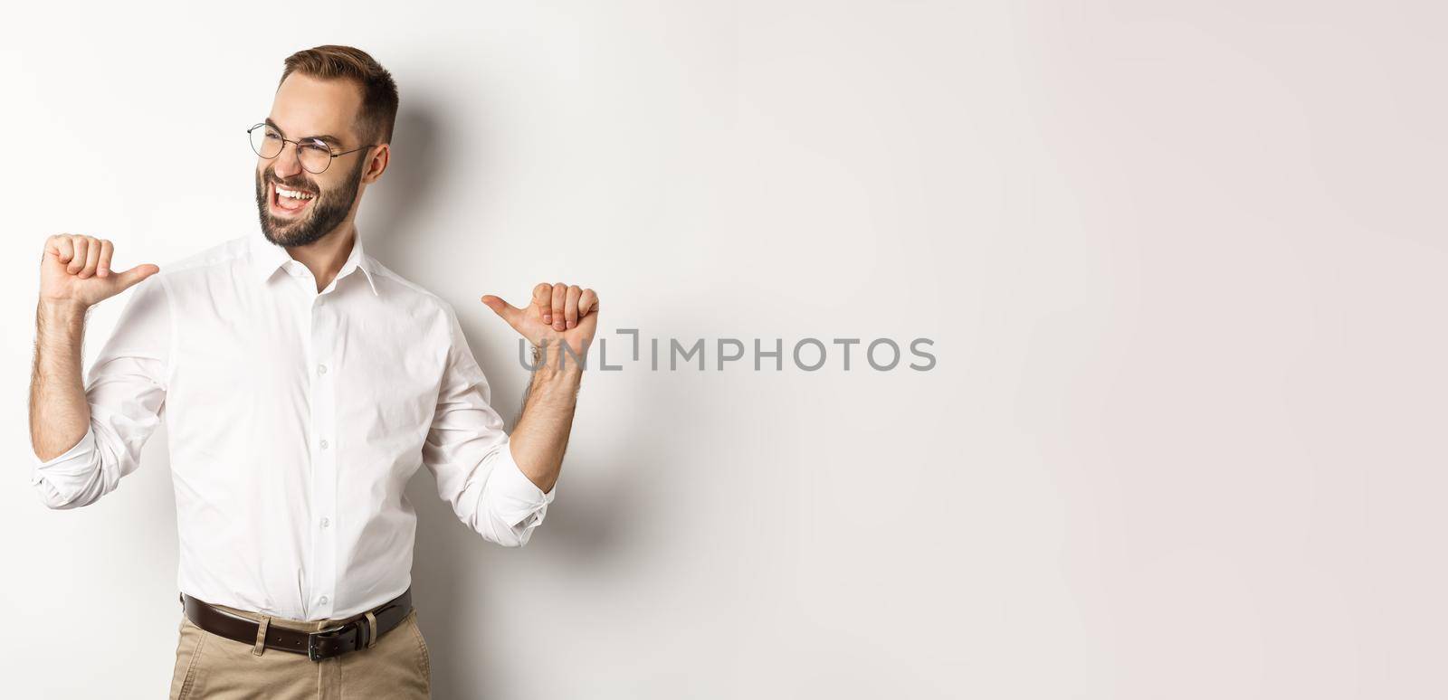 Satisfied and self-assured businessman pointing at himself, standing over white background.