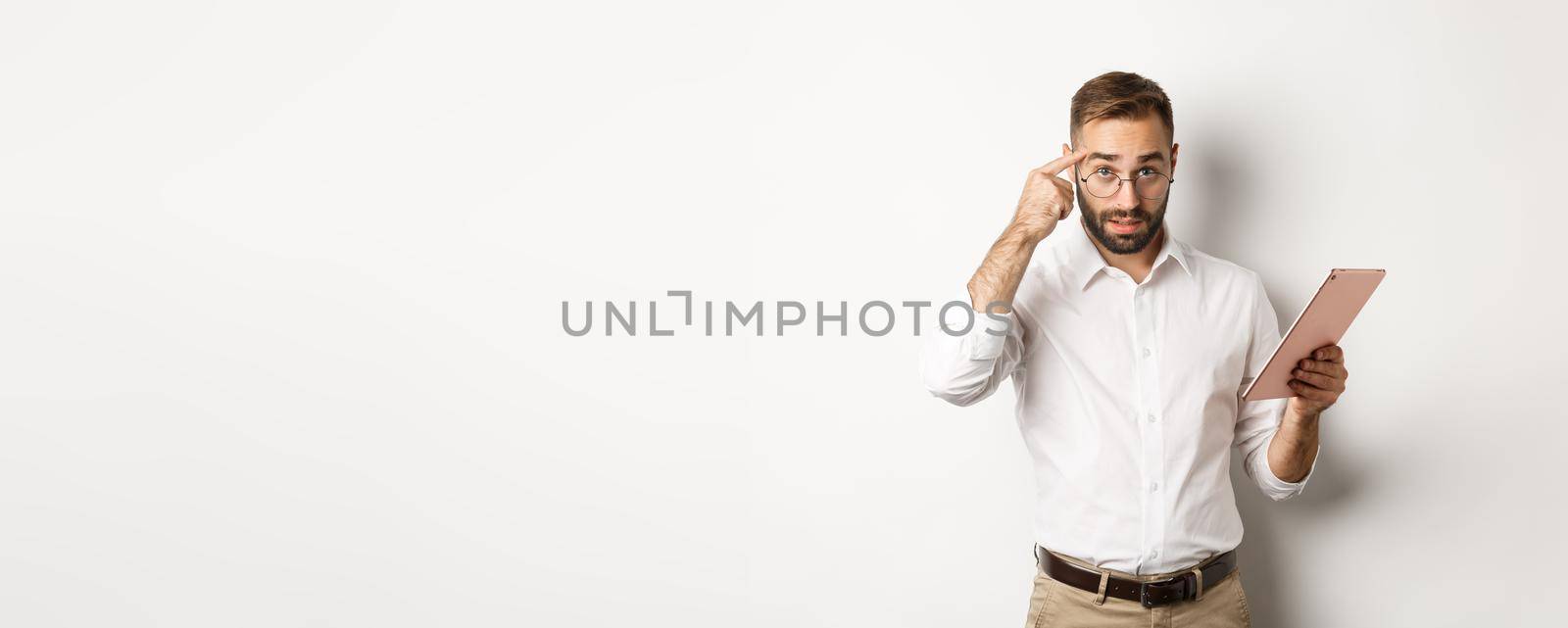 Displeased employer scolding staff while checking report on digital tablet, pointing at head and looking disappointed, standing over white background.