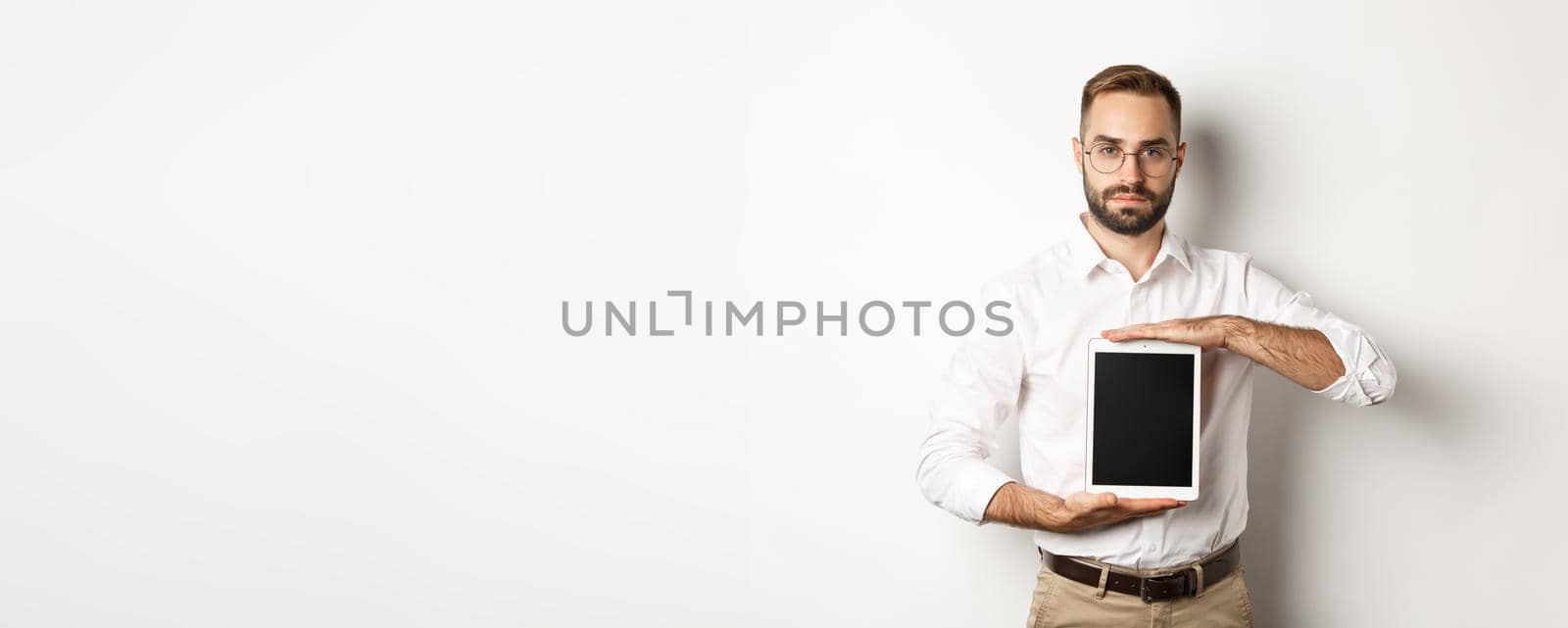 Confident bearded man showing digital tablet screen, demonstrating app, standing over white background.