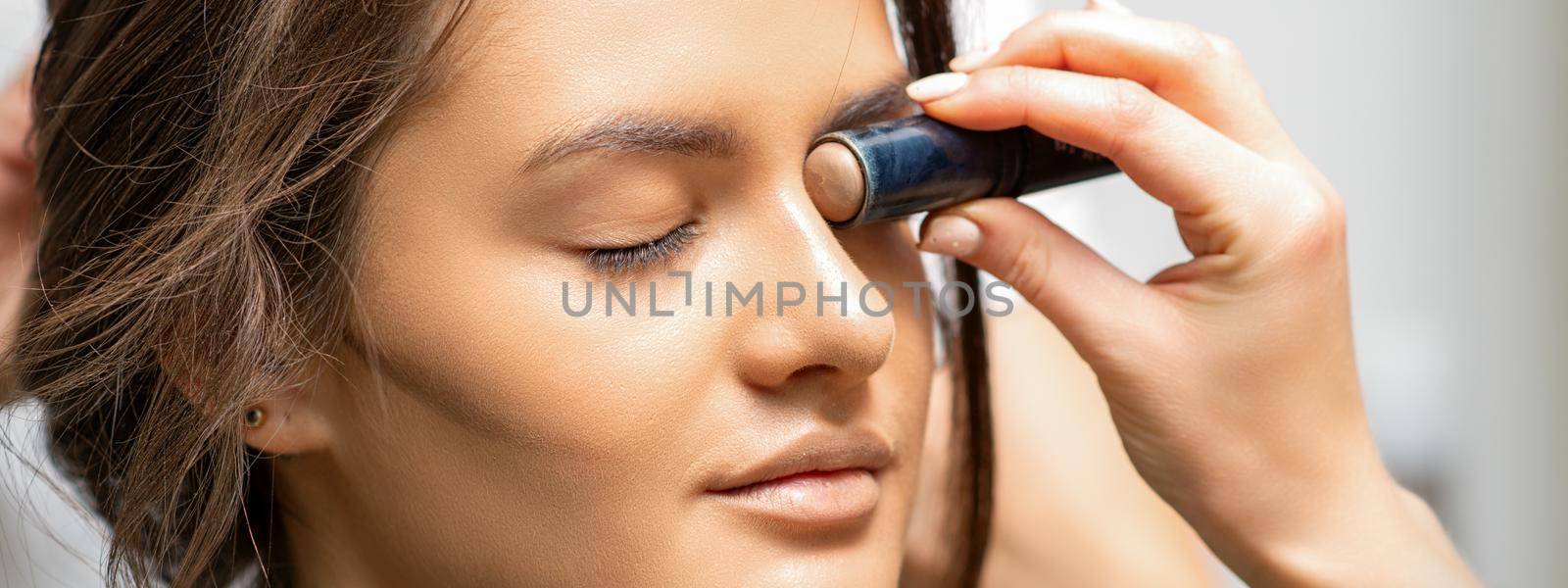 Make up artist contouring the face of a young woman with cream blush close up