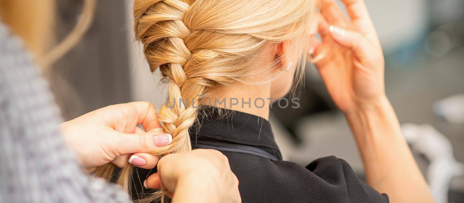 Braiding braid. Hands of female hairdresser braids long braid for a blonde woman in a hair salon