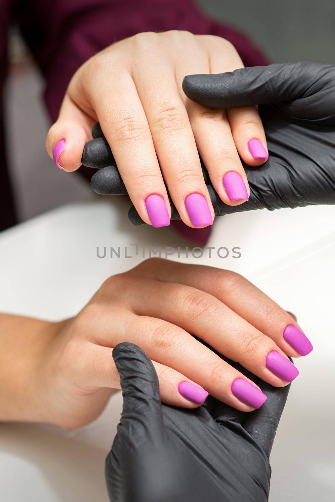 Examination of manicured fingernails. Hands of manicure master in black gloves examining female pink nails in manicure salon. by okskukuruza