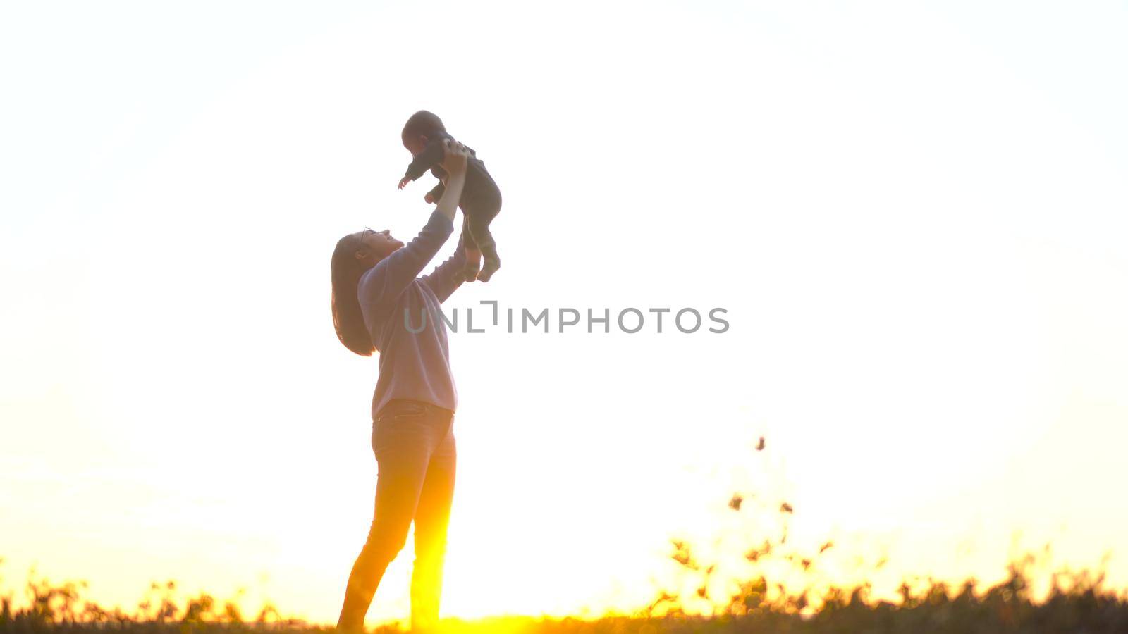 A young woman holds a baby in her arms against the background of a sunset. Mom and son on the hill. 4k