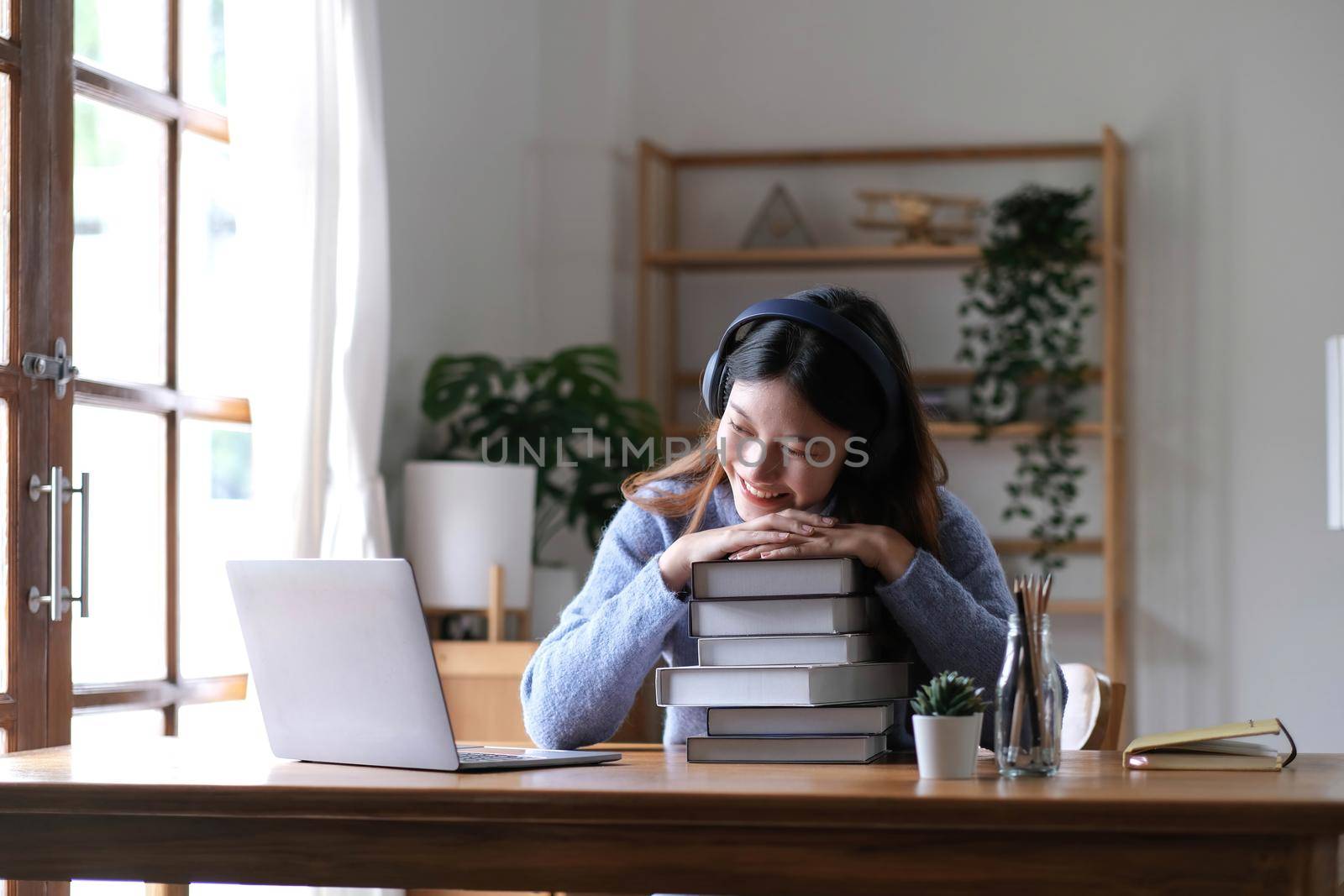 Smiling Asian woman using headset looking at laptop screen listen and learn online courses with a video call with headphones for online learning by wichayada