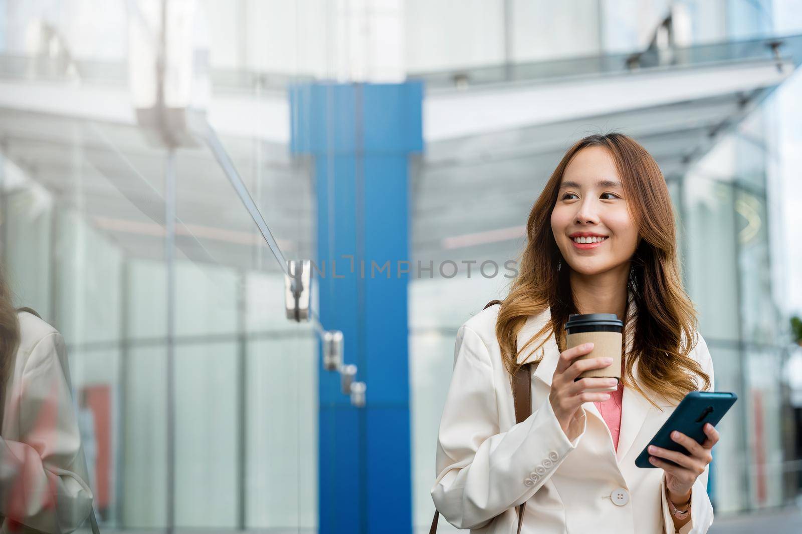Asian businesswoman with smartphone and cup coffee standing street front building near office, Portrait woman smiling holding smart mobile phone with coffee take away going to work early in morning