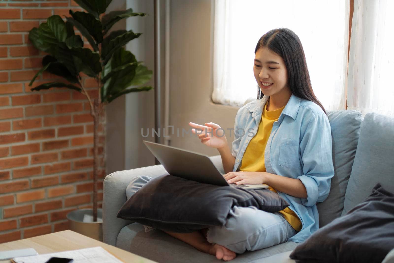 Happy young girl having video call on laptop, studying online, communicating with friends, consulting, or explainging while sitting confortably on couch at home. Online learning and distant working concept.