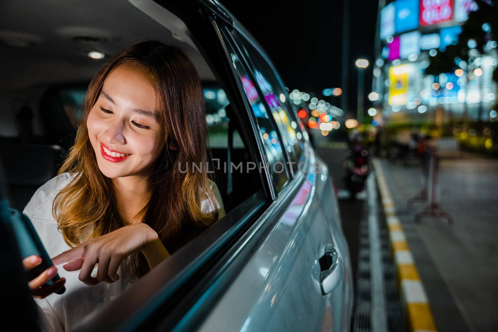 Happy beautiful woman texting smartphone sitting car back seat in urban, Asian businesswoman working late commuting from office in Taxi backseat with mobile phone in city at night after late work