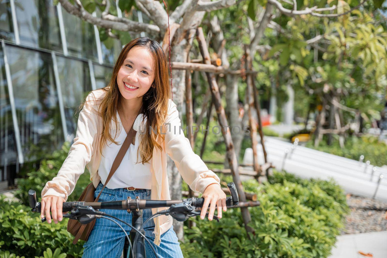 Happy Asian young woman riding bicycle on street outdoor near building city by Sorapop