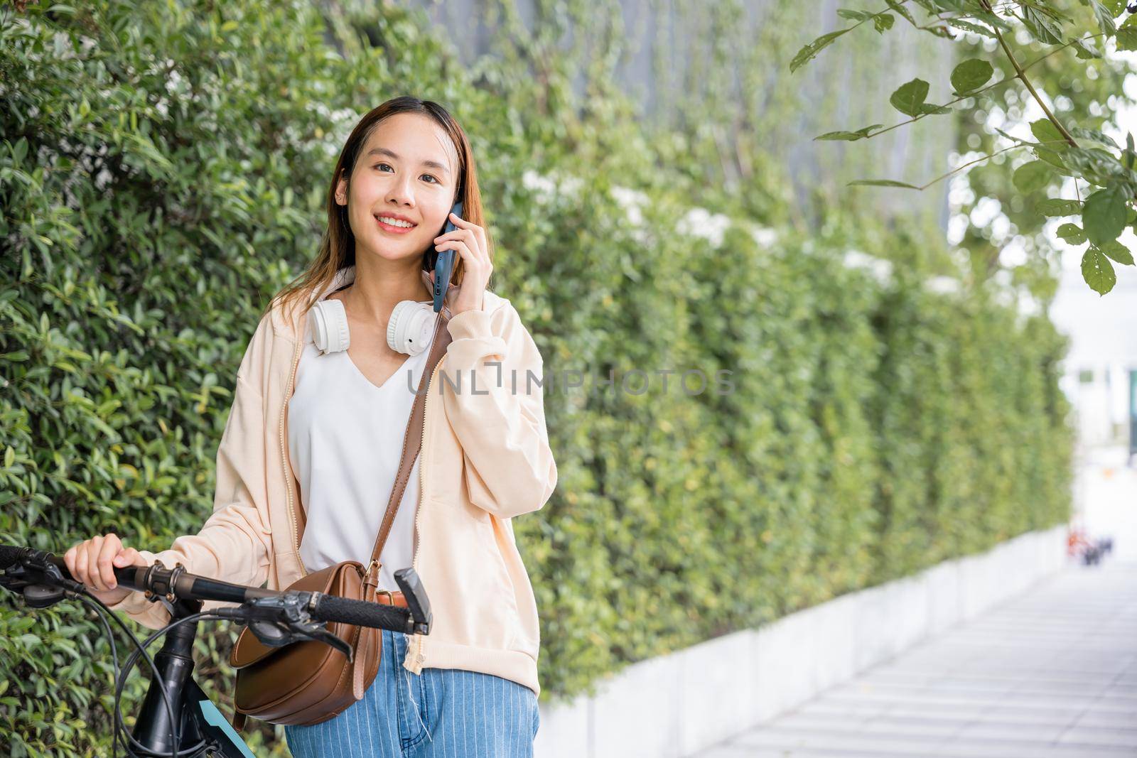 woman walking in countryside outdoor with her bicycle she using mobile phone talking with friend by Sorapop