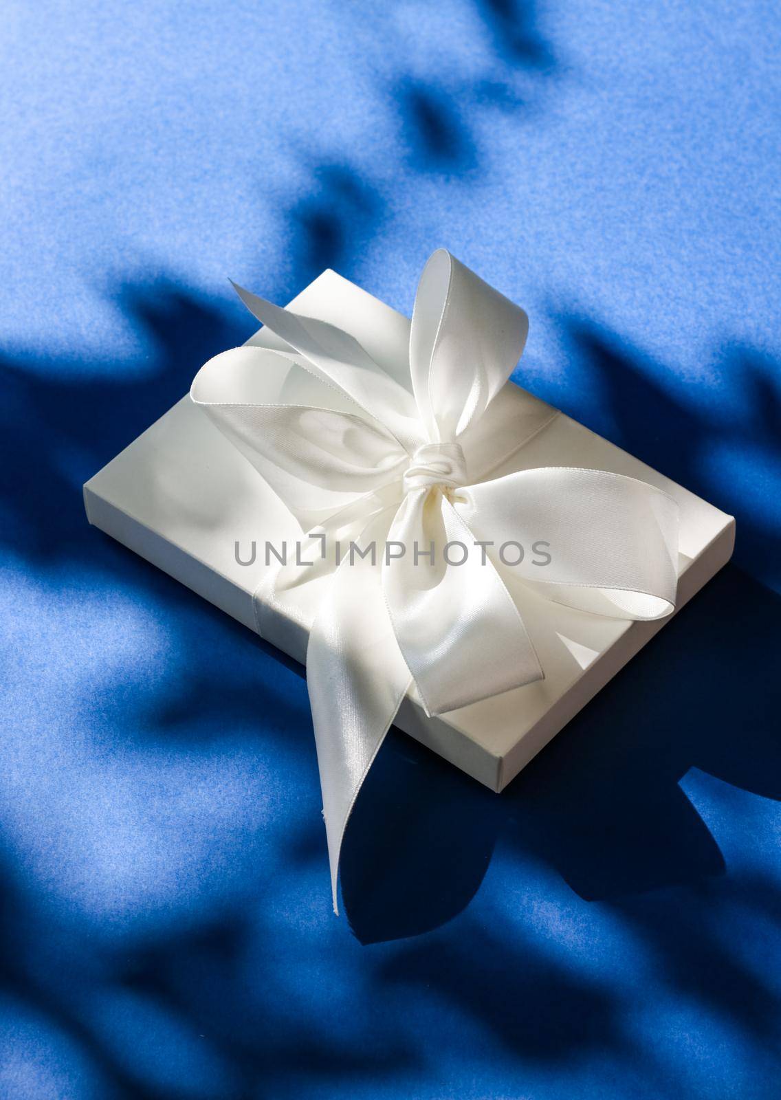 Anniversary celebration, shop sale promotion and bridal surprise concept - Luxury holiday white gift box with silk ribbon and bow on blue background, luxe wedding or birthday present