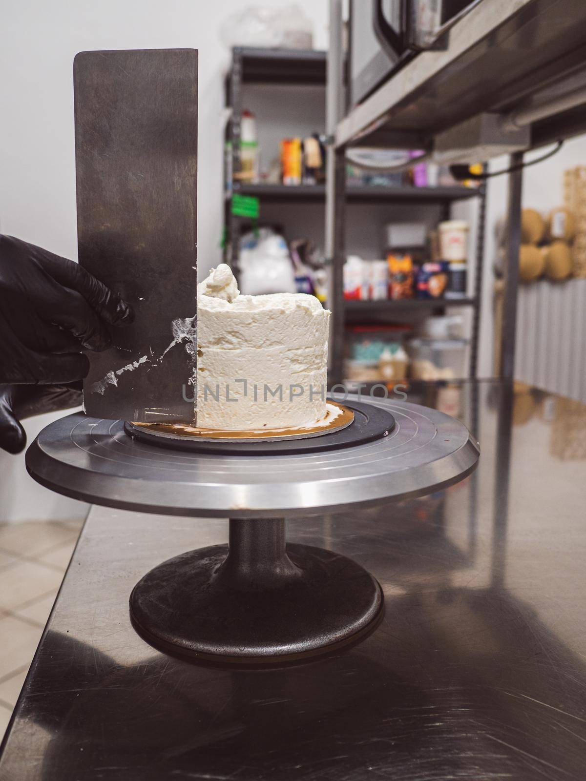 Decorator using spatula and scraper to smooth buttercream on a frosted cake