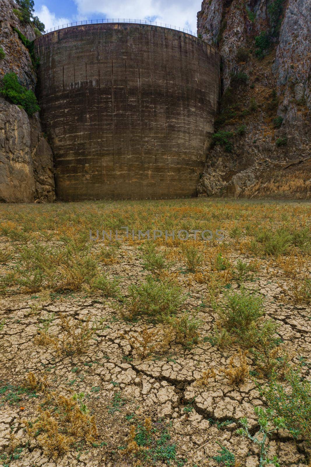 dry swamp bottom with cracked earth, in the background the dam without water due to drought sky with storm clouds