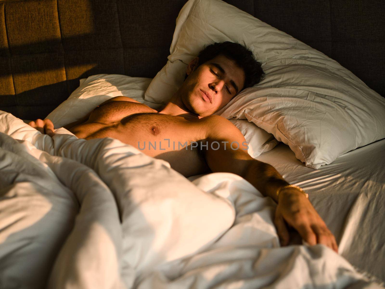 Handsome shirtless athletic young man laying in bed at night with eyes closed, sleeping