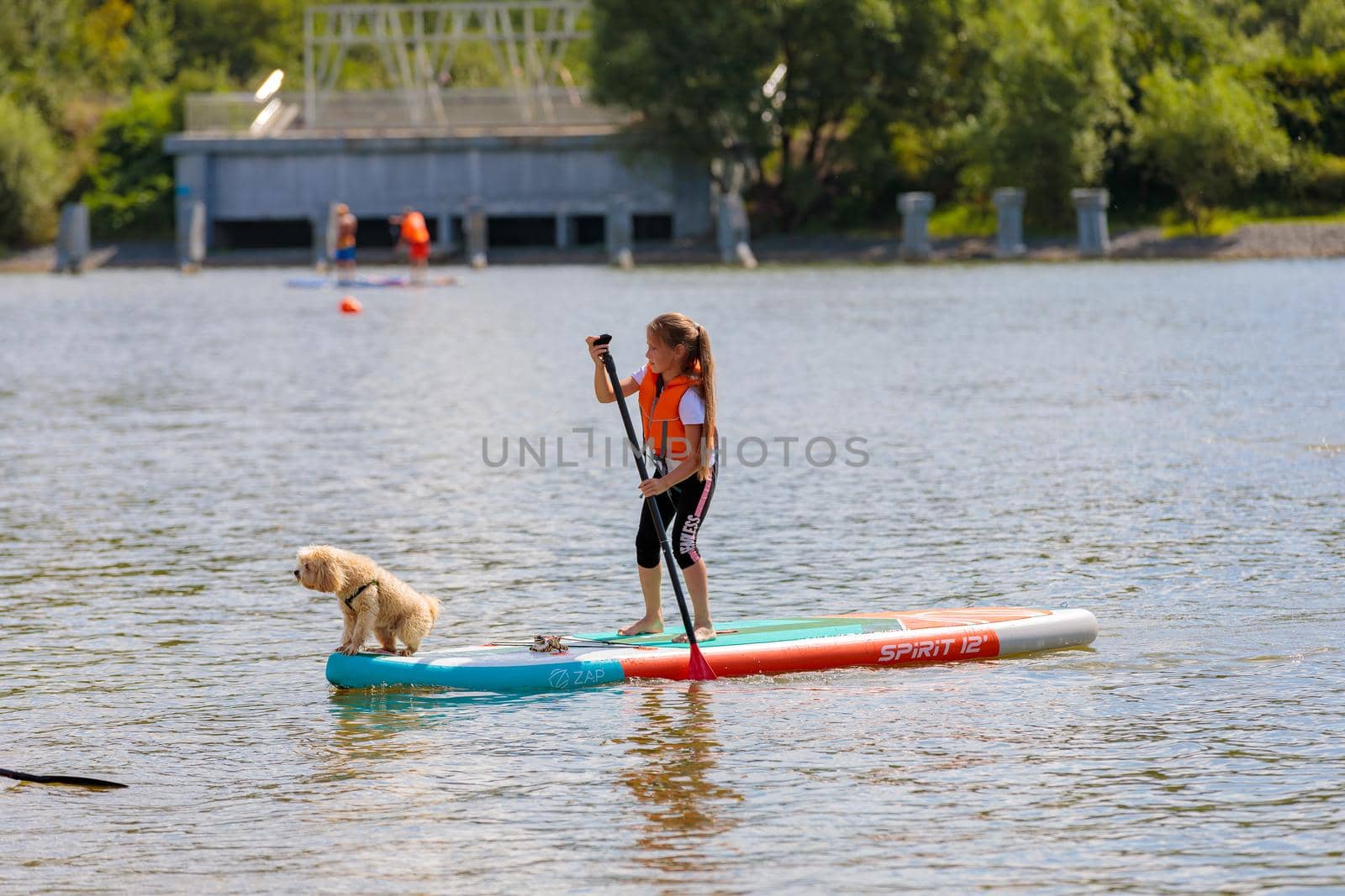 A child with a dog swims on a surfboard, pushing off with a paddle. Paddleboarding. Russia Zelenograd 14 August 2021