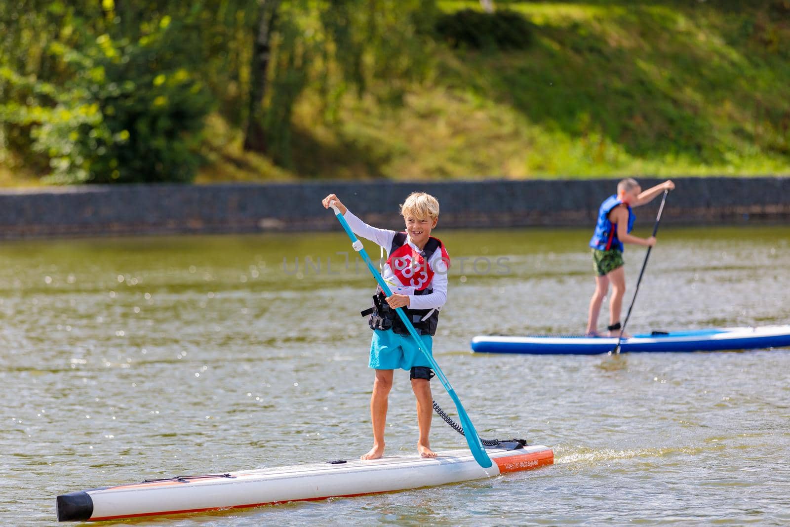 A child swims on a surfboard, pushing off with a paddle. Paddleboarding. Russia Zelenograd 14 August 2021