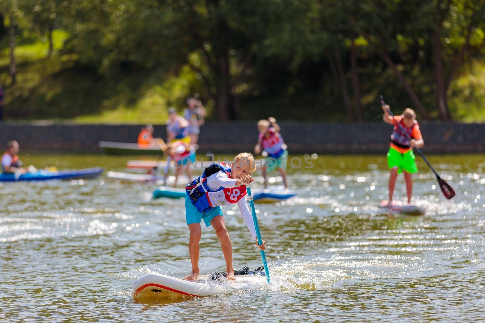 A child swims on a surfboard, pushing off with a paddle. Paddleboarding. Russia Zelenograd 14 August 2021