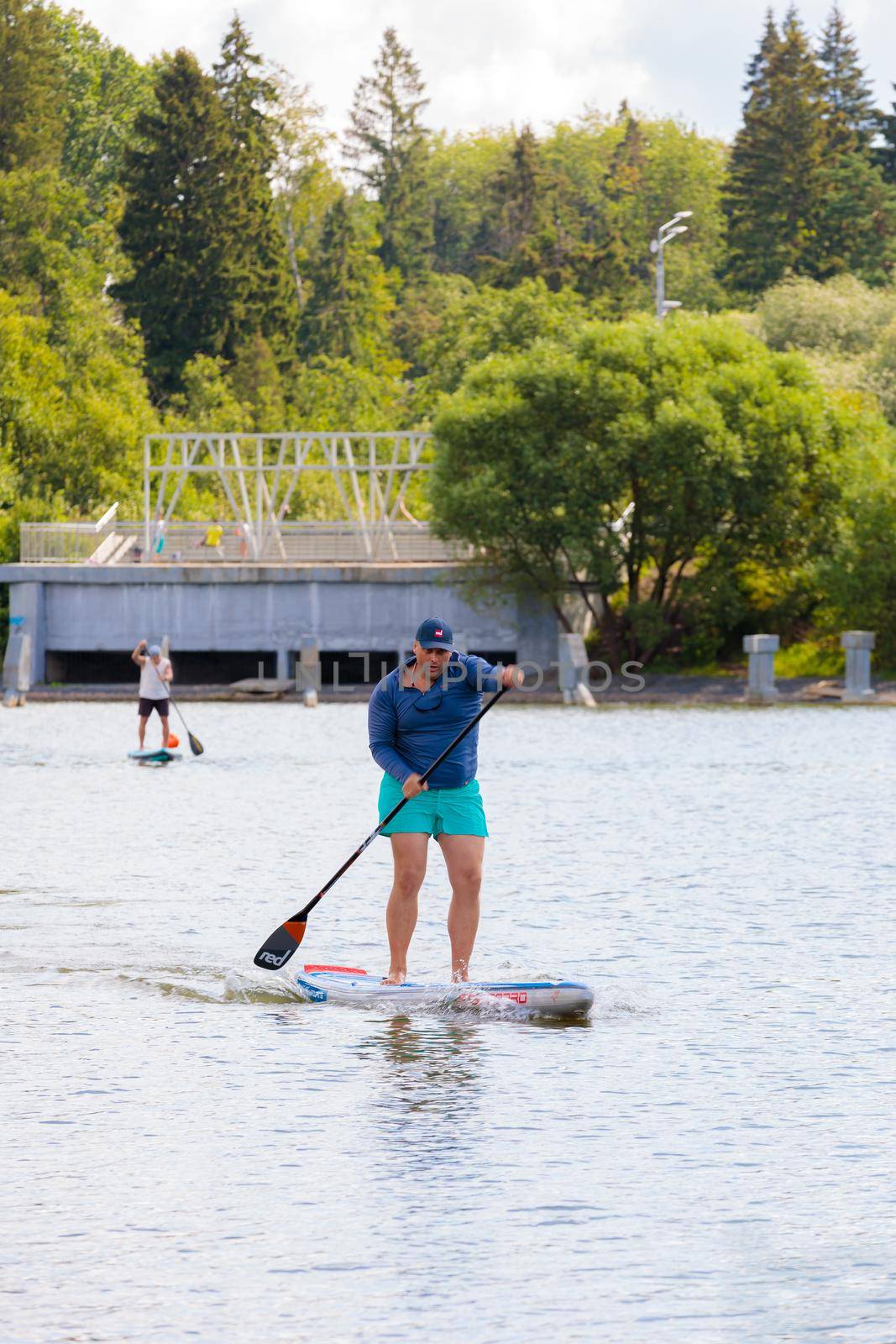 A man swims on a surfboard, pushing off with an oar. Paddleboarding. Russia Zelenograd 14 August 2021