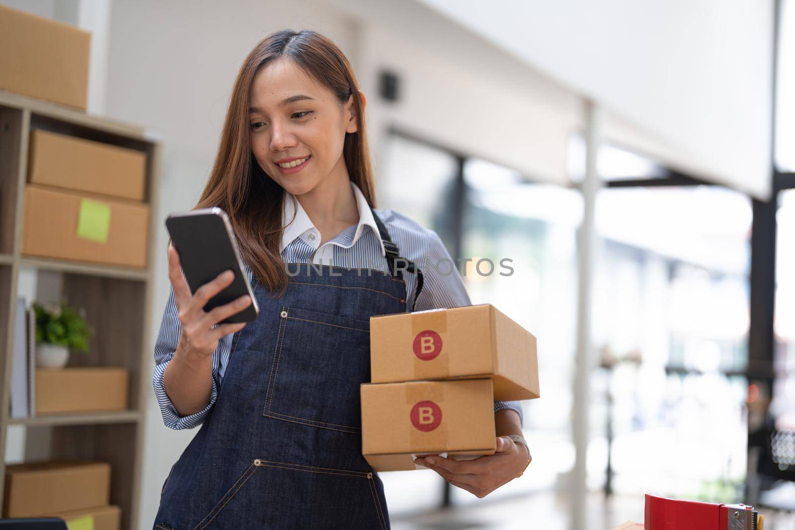 small stock business owner holding phone and retail package parcel boxes checking commercial shipping delivery order on smartphone using mobile app technology. by nateemee