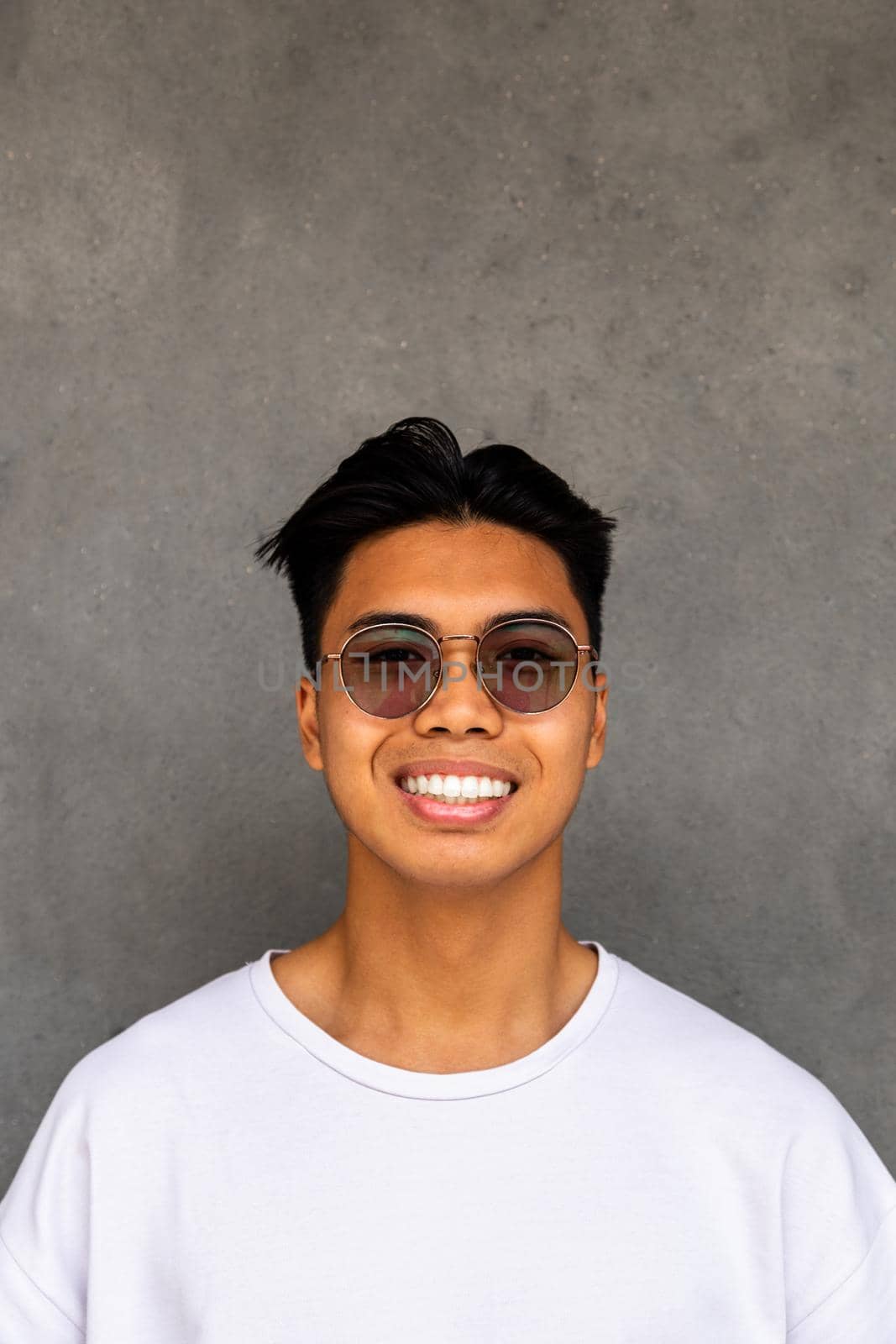 Smiling teen asian boy with glasses looking at camera. Dark concrete wall background. Vertical image. Lifestyle concept.