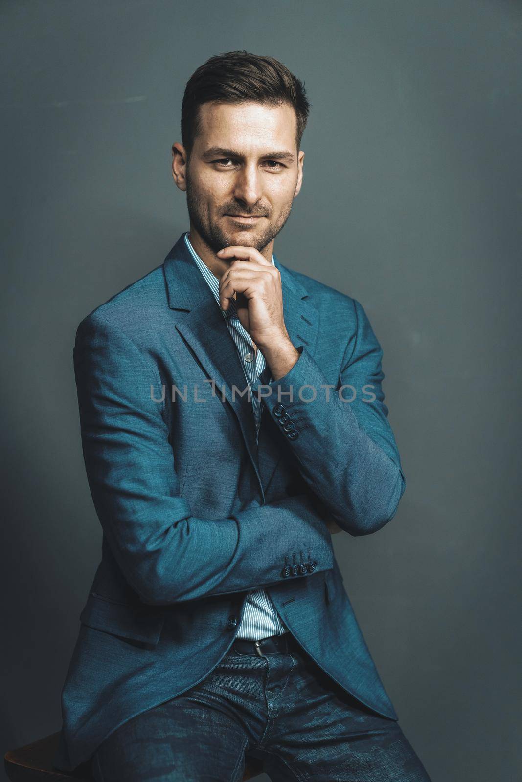 Elegance Businessman in a Blue Formal Waist Up Suit Jacket Gazes Straight to the Camera. Elegant Brown Haired Man Posing in Studio on a Gray Background. . High quality photo