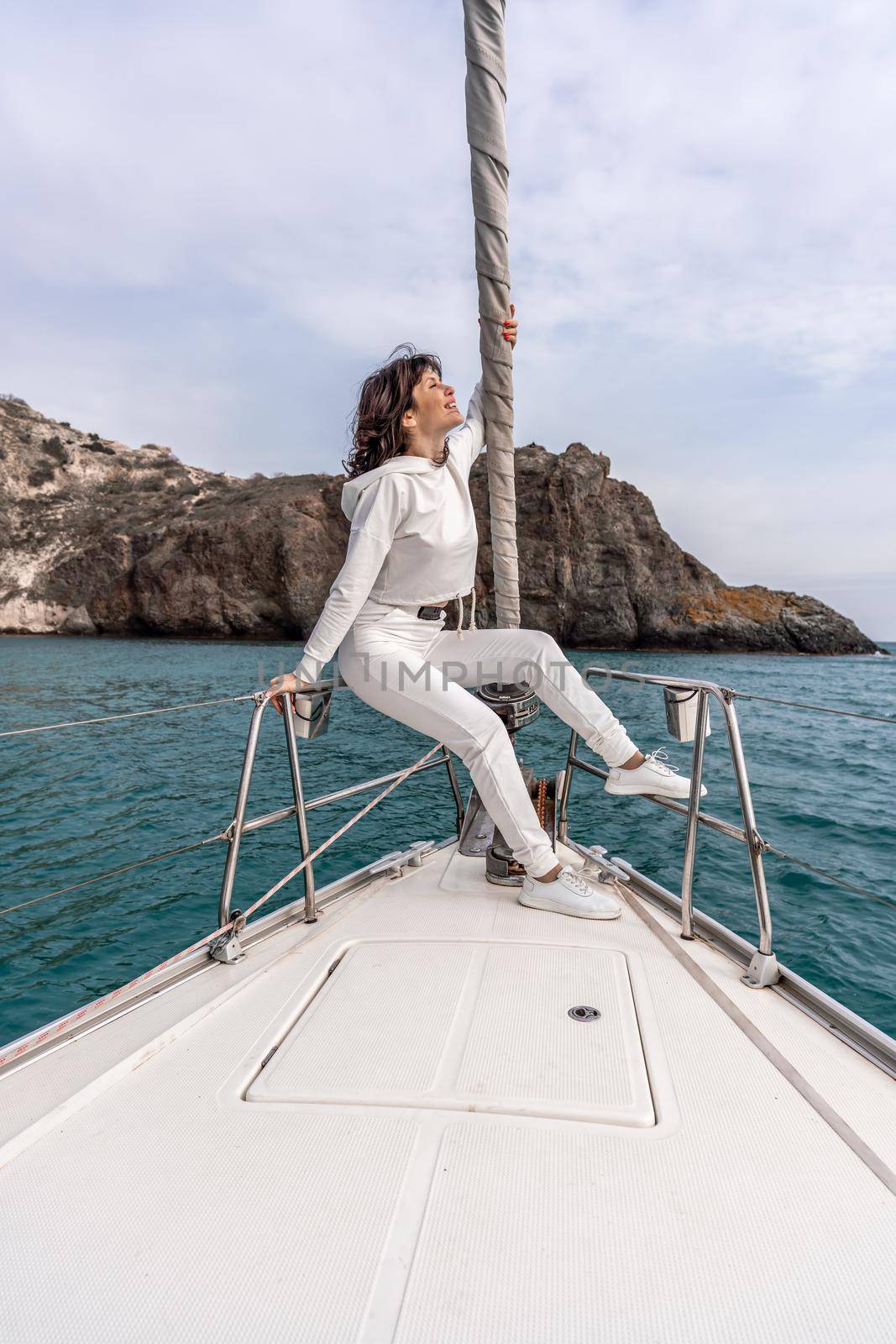 Woman standing on the nose of the yacht at a sunny summer day, breeze developing hair, beautiful sea on background by Matiunina