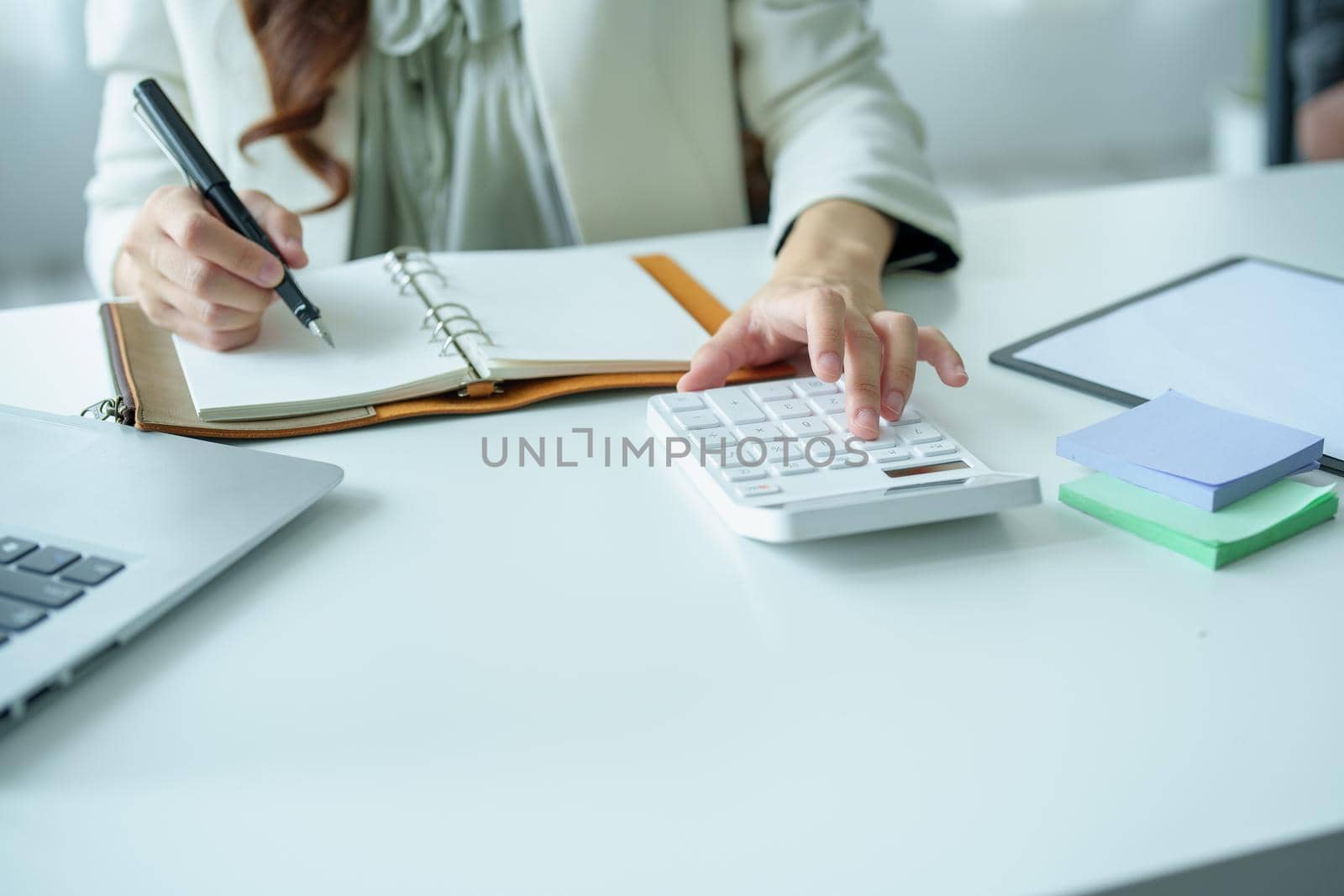 Portrait of an Asian bank employee using a financial budget calculator, notepad and computer to working.