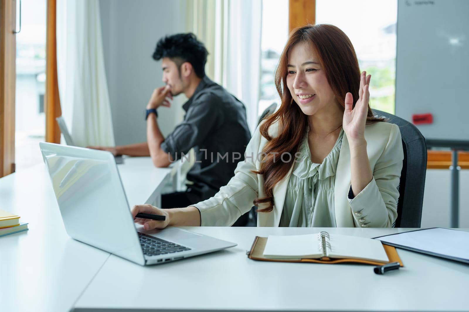 Portrait of an Asian bank employee using a laptop video conferencing with team members working on budget paperwork at their desk in their office.