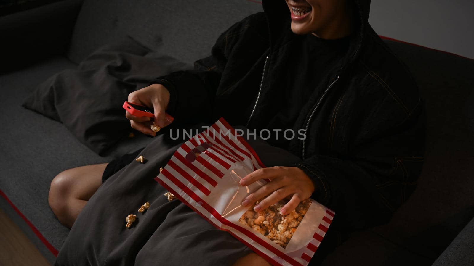 Happy man with remote control eating popcorn and watching movie in living room. Entertainment and leisure activity concept by prathanchorruangsak