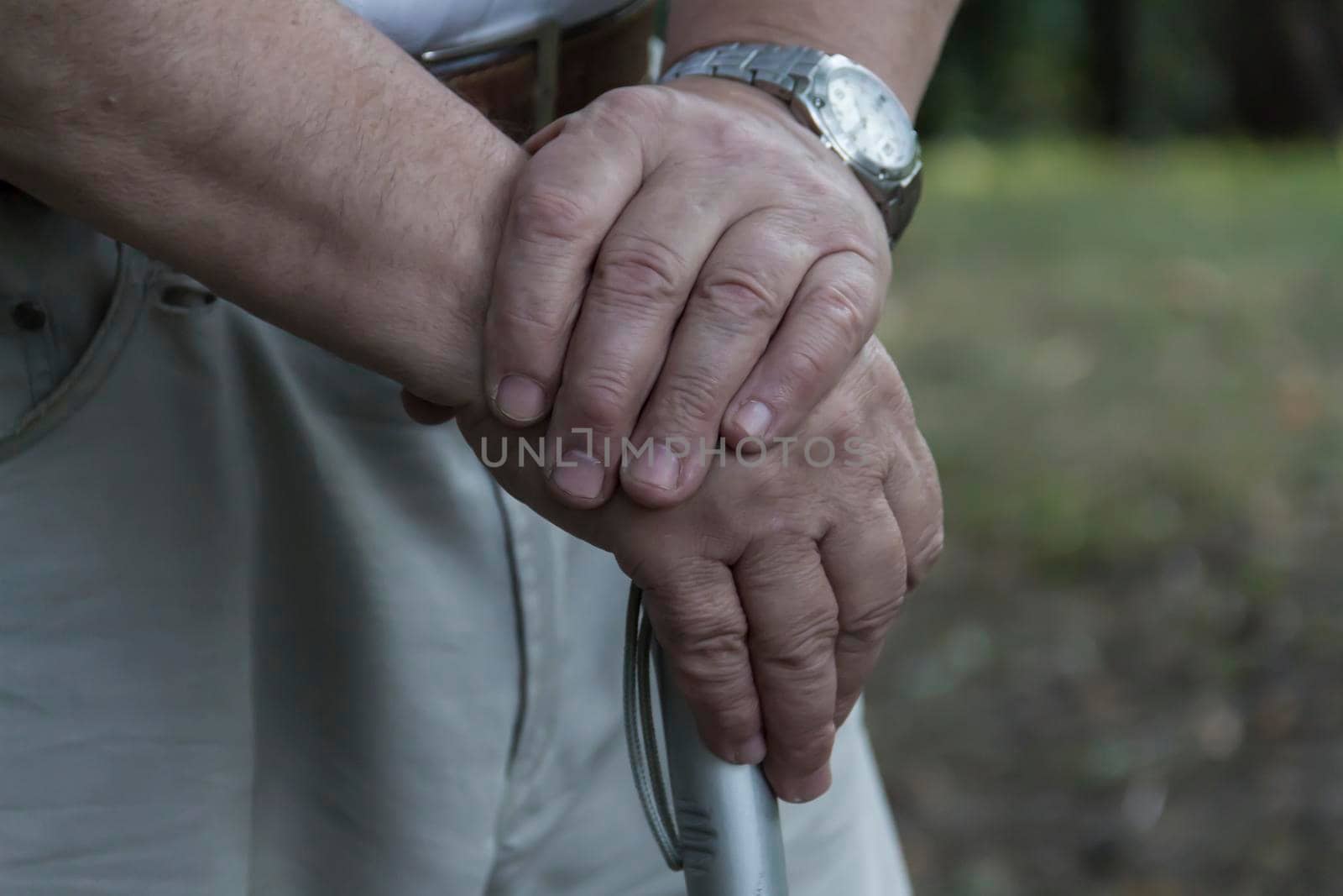 The large hands of an elderly man are folded on a cane with a watch on his right hand by Alla_Yurtayeva