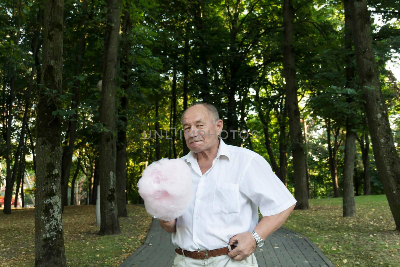 An old retired man in a white shirt walks with a huge, pink, cotton candy on the path in the park by Alla_Yurtayeva