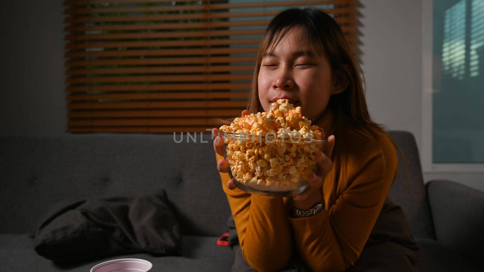 Smiling young woman enjoy eating popcorn and watching movie at home. Entertainment and leisure activity concept.