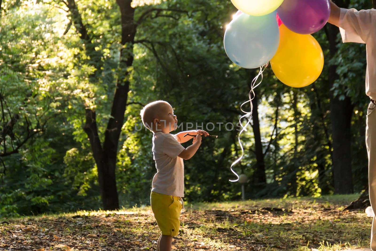 A little boy in yellow shorts and an elderly old man are playing with bright balloons. The family is having fun in the park in the fresh air and celebrating the holiday..