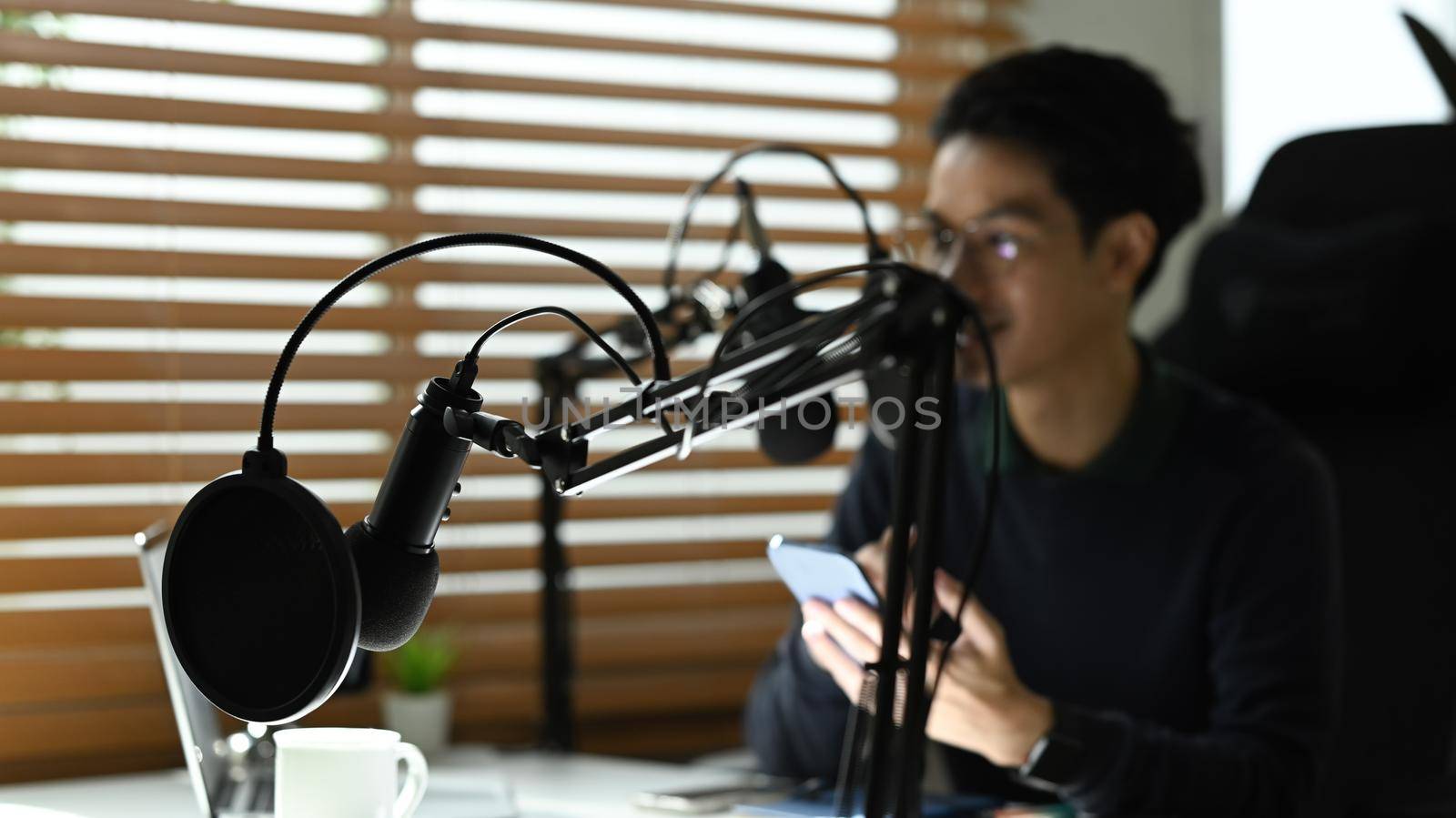 Young podcaster using a microphone and laptop computer recording audio for channel in home studio.