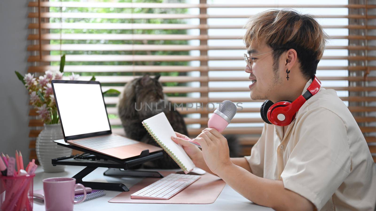 Young podcaster using a microphone and laptop computer recording audio for channel in home studio.