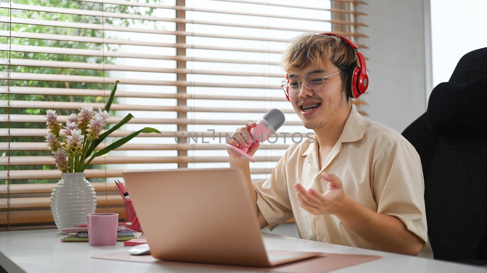 Young podcaster using a microphone and laptop computer recording audio for channel in home studio.