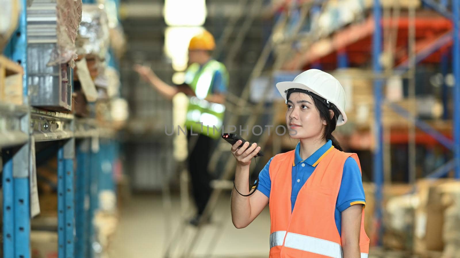 Warehouse workers in safety uniform working in warehouse full of tall shelves with goods in cardboard boxes.