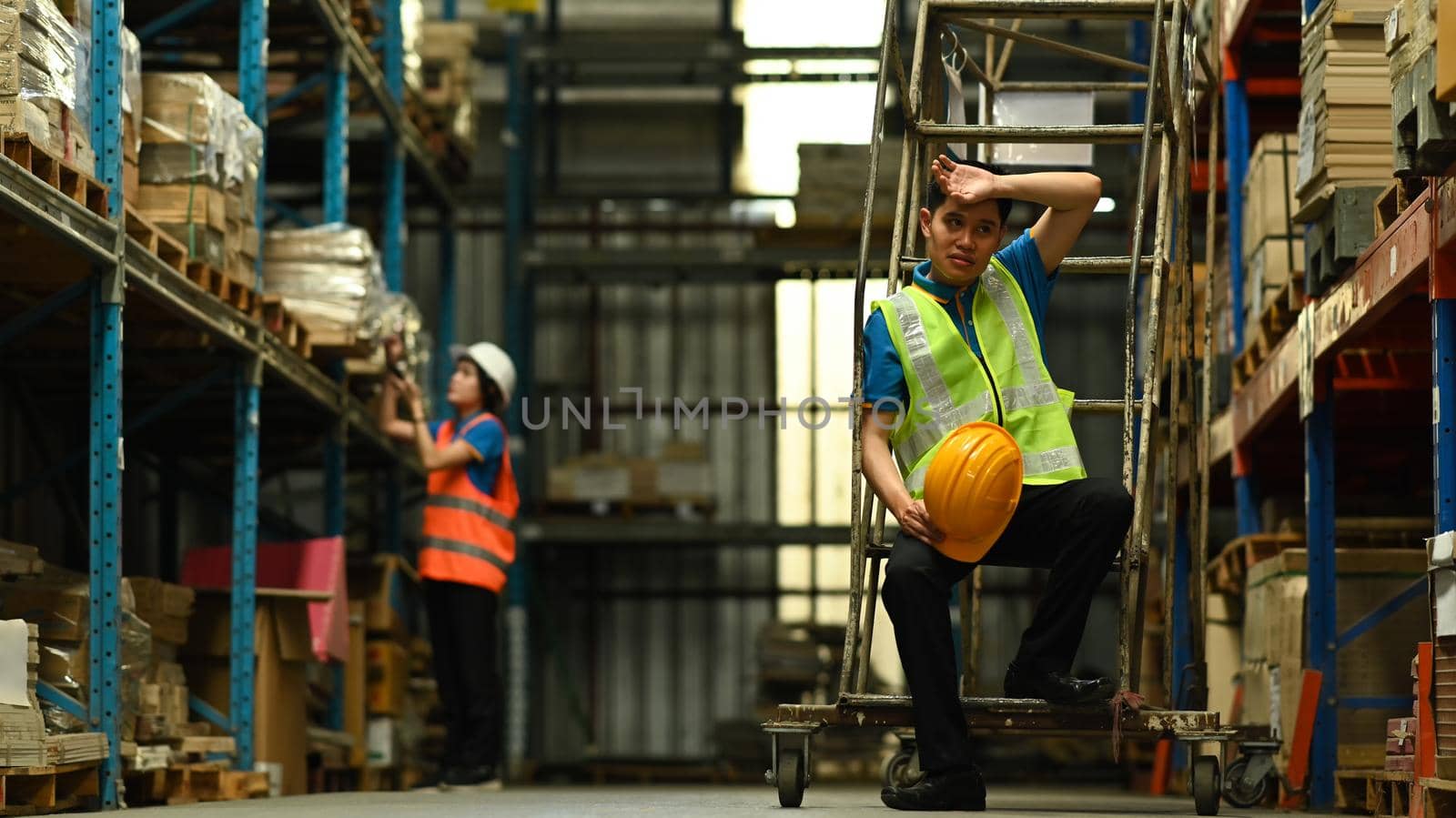 Warehouse workers in safety uniform working in warehouse full of tall shelves with goods in cardboard boxes.