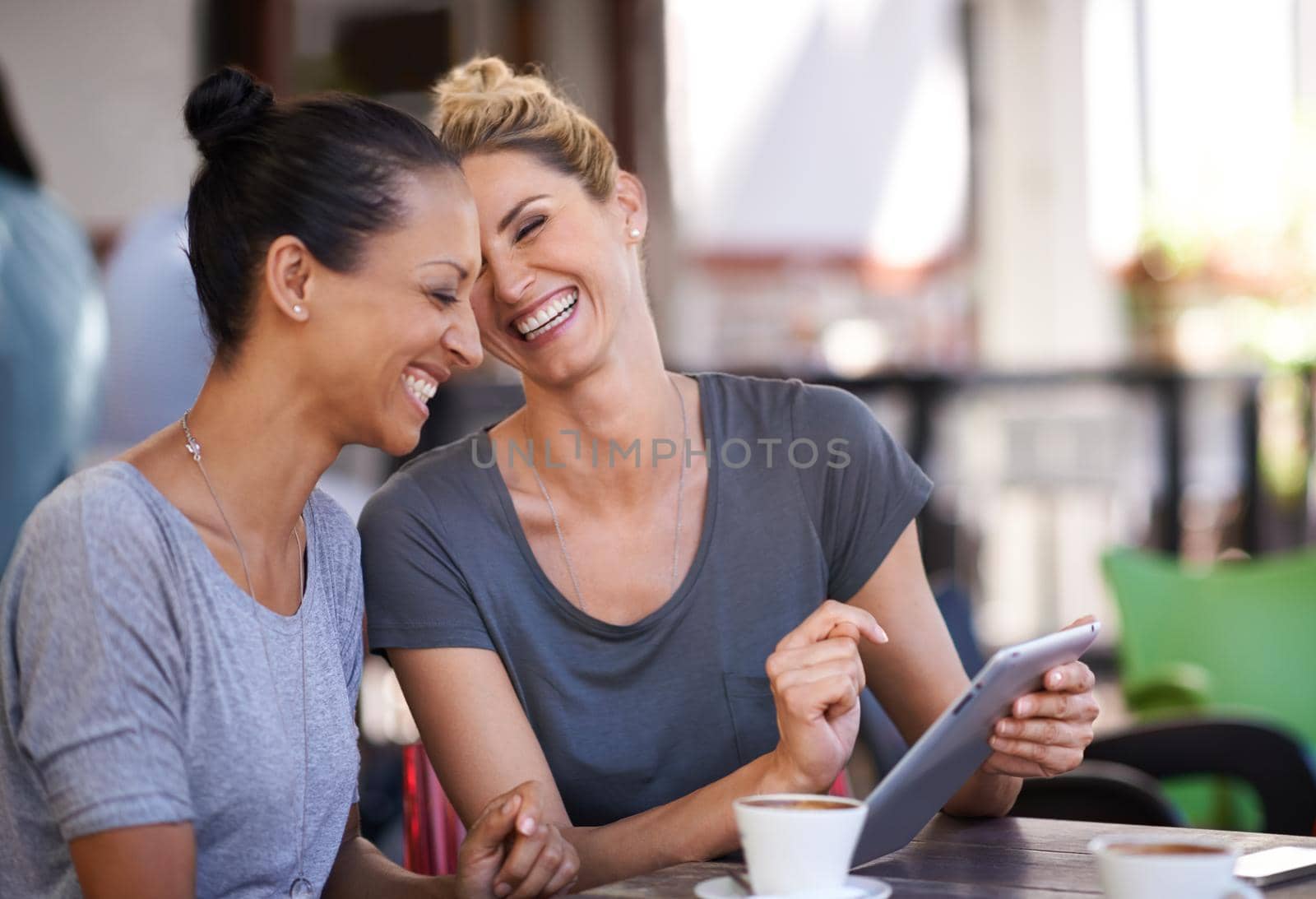 Technology brings people closer. Two young women looking at a tablet in a coffee shop. by YuriArcurs